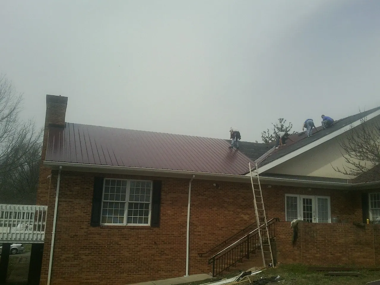 Crew setting red metal roofing panels on a brick home in Greenville